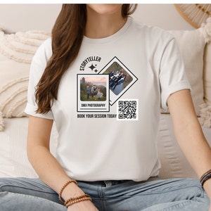 May include: White t-shirt with a black and white design featuring a photo of a family in front of a castle, the text "Storyteller", "DMK Photography", and "Book your session today", and a QR code.
