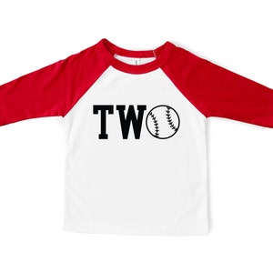 May include: White and red baseball raglan shirt with black text that says "TWO" and a black baseball graphic.