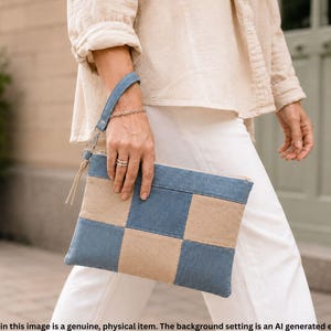 May include: A rectangular zippered clutch bag featuring a patchwork design of alternating denim blue and beige fabric squares. The clutch includes a matching denim blue wrist strap attached to a metal zipper pull with a thin fabric cord detail.