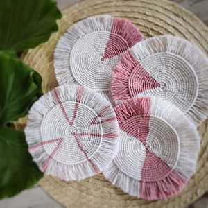 May include: Four crocheted coasters with a white center and pink trim. The coasters have a circular shape and are made with a macrame technique.