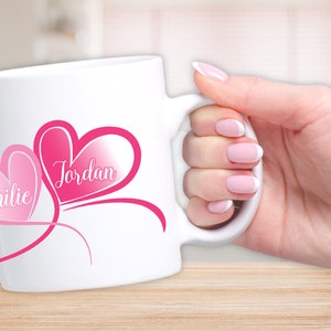 Op de afbeelding: Witte keramische mok met roze harten en de namen "Jordan" en "Millie" in cursief.