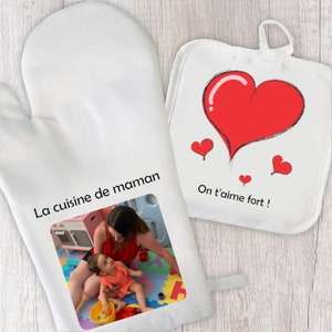 Può includere: Due guanti da forno bianchi con un design a forma di cuore rosso e il testo "On t'aime fort!" Un guanto presenta una foto di una madre e un bambino che giocano. L'altro guanto ha il testo "La cuisine de maman".