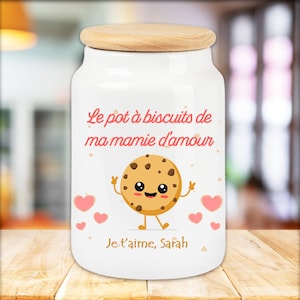 Peut inclure: Pot à biscuits en céramique blanche avec un couvercle en bois. Le pot a un biscuit dessin animé avec un visage souriant et le texte "Le pot à biscuits de ma mamie d'amour Je t'aime, Sarah".