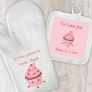 Può includere: Set di guanto da forno e presina bianchi. Il guanto presenta una grafica di cupcake rosa e il testo "Les bons gâteaux de mamie Annick". La presina ha uno sfondo rosa con una grafica di cupcake e il testo "On t'aime fort, Johnny, Eva & Jade".
