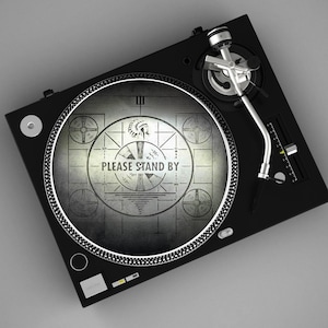 May include: A black turntable with a silver tone arm and a circular record. The record features a retro graphic with the text "PLEASE STAND BY". The turntable is set against a gray background.