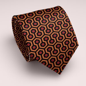 May include: A necktie featuring a repeating geometric pattern of interlocking orange and black hexagons with dark red circular centers. The tie is folded over itself, displaying the consistent, symmetrical print across the fabric surface.