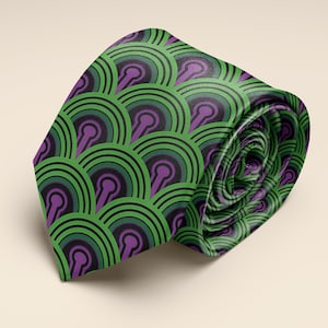 May include: Rolled necktie with a repeating pattern of green, black, and purple semi-circles. The tie is a vibrant green with a repeating pattern of black and purple shapes. The tie is rolled up, showing the pattern in a spiral.