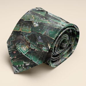 May include: A rolled necktie featuring a repeating pattern of green and brown circuit boards. The tie is a dark green color with a complex design, and is set against a neutral background.