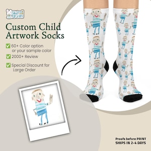 May include: A pair of white crew socks featuring a repeating pattern of a child's drawing of a person wearing a blue striped shirt and blue pants. The socks have black toe and heel sections. The image includes text: Custom Child Artwork Socks.