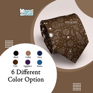 Peut inclure: Une cravate marron ornée d'un motif spatial blanc avec des planètes, des fusées et des astronautes. L'image présente également six options de couleurs : noir, café, marine, cola, aubergine et patine. Le texte indique "6 Options de couleurs différentes".