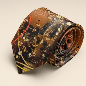 May include: Rolled necktie with a brown circuit board design. The tie features a detailed print of electronic components, including resistors, capacitors, and wiring, in shades of brown, yellow, and red. The tie is rolled up, showcasing its pattern.