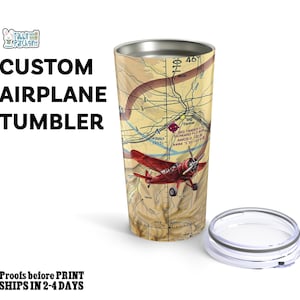 May include: A stainless steel tumbler featuring a map design and a red airplane graphic. The tumbler has the words "CUSTOM AIRPLANE TUMBLER" printed on it. The clear lid is placed beside the tumbler.