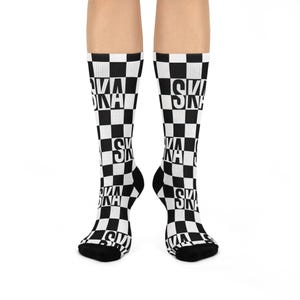 May include: A pair of black and white checkered socks. The socks feature the word "SKA" in white block letters, repeated in a checkerboard pattern. The socks are knee-high and have black heels and toes.