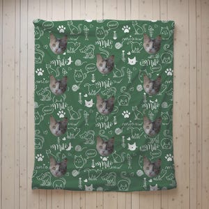 May include: A green blanket featuring a repeating pattern of white line drawings of cats, fish bones, yarn balls, and paw prints. The design includes the name Milo in a script font and the word miauw, interspersed with photos of a cat.