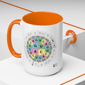 Pode incluir: Caneca de cerâmica branca com interior e alça laranja. A caneca apresenta um design circular colorido com elementos de código genético e texto. Um presente com tema científico.
