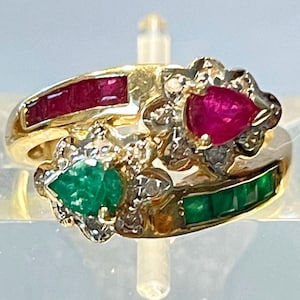 Może przedstawiać: Złoty pierścionek z czerwonym rubinem, zielonym szmaragdem i diamentami. Pierścionek jest osadzony w kwiatowym wzorze.