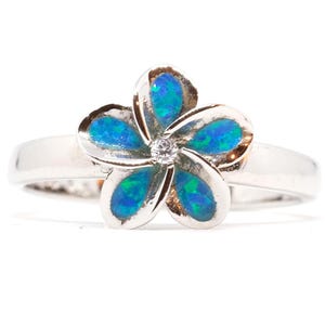 May include: A silver ring featuring a flower design with five petals. Each petal is filled with blue and green opal-like material. A small, clear gemstone is set in the center of the flower.