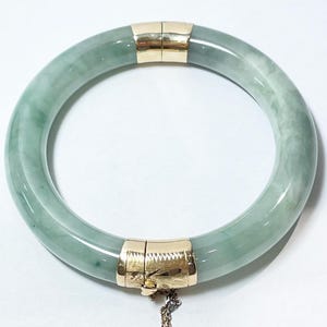 Può includere: Un braccialetto di giada verde con una chiusura in oro. Il braccialetto è realizzato in giada liscia e lucida e ha un design semplice ed elegante.