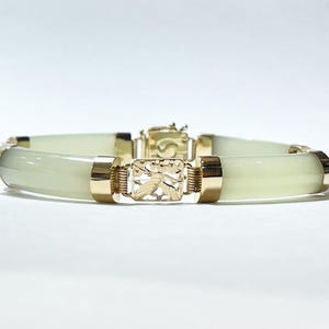 May include: A jade and gold bracelet with a delicate floral design. The bracelet is made of smooth, light green jade and features a gold clasp with a floral pattern.