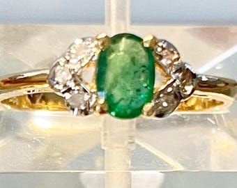 May include: A gold ring with a large oval emerald gemstone surrounded by smaller diamonds.