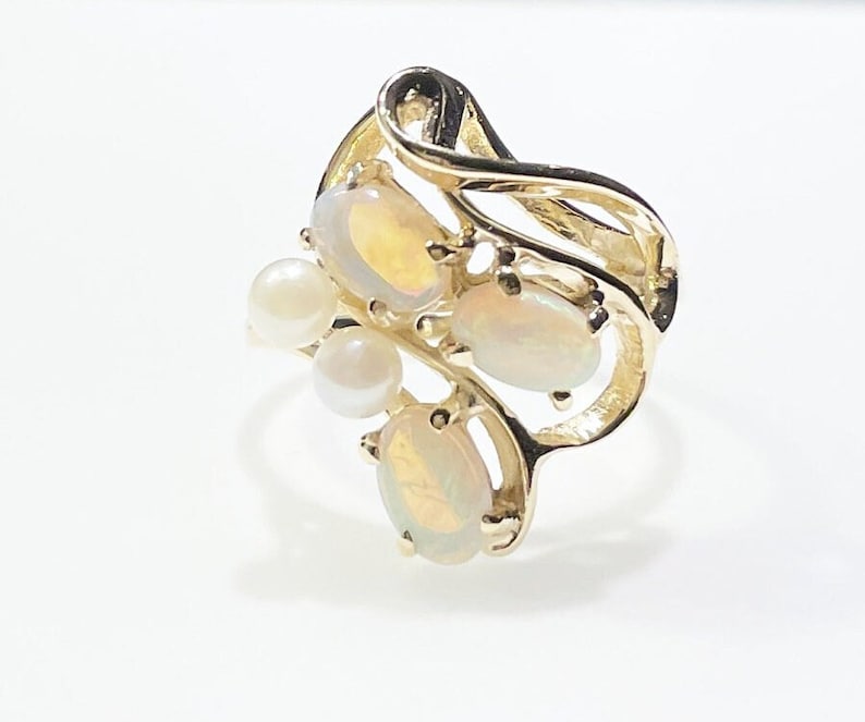 Pu&ograve; includere: Un anello d'oro con un design a spirale incastonato con tre opali ovali e tre perle bianche.