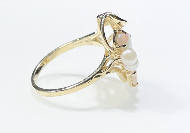 Pu&ograve; includere: Un anello d'oro con un gruppo di perle bianche e una pietra di opale. L'anello &egrave; incastonato in un design delicato e intricato.