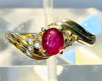 May include: A gold ring featuring a large oval ruby gemstone and smaller diamonds set in the band.