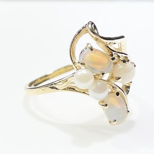 Pu&ograve; includere: Un anello d'oro con un gruppo di opali e perle. L'anello ha un design delicato e a spirale.