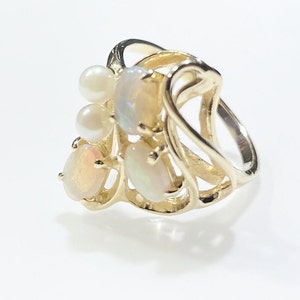 Pu&ograve; includere: Un anello in oro con un design delicato che presenta pi&ugrave; opali e perle di forma ovale. L'anello ha una forma unica e fluida.