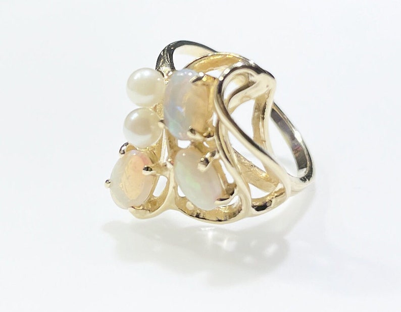 Pu&ograve; includere: Un anello in oro con un design delicato che presenta pi&ugrave; opali e perle di forma ovale. L'anello ha una forma unica e fluida.