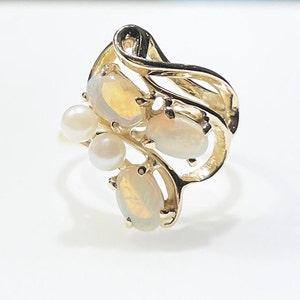 Pu&ograve; includere: Un anello d'oro con tre opali ovali e due accenti di perle. L'anello ha un design delicato e fluido.