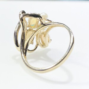 Pu&ograve; includere: Un anello d'oro con un gruppo di pietre di opale e perle incastonate in un design delicato e a spirale.