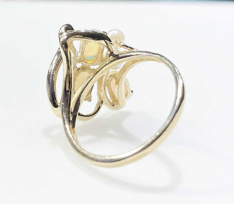 Pu&ograve; includere: Un anello d'oro con un gruppo di pietre di opale e perle incastonate in un design delicato e a spirale.