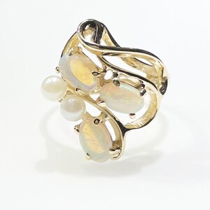 Pu&ograve; includere: Un anello d'oro con un design a spirale incastonato con tre opali ovali e tre perle bianche.