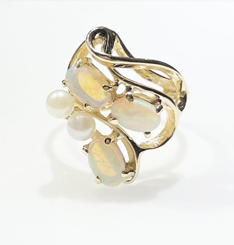 Pu&ograve; includere: Un anello d'oro con un design a spirale incastonato con tre opali ovali e tre perle bianche.