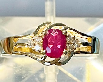 May include: A gold ring featuring a large oval ruby gemstone and two smaller diamond accents. The ring has a delicate, intricate design.