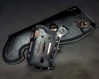 Könnte beinhalten: Ein Köcher und ein passender Armschutz aus schwarzem lederähnlichem Material. Der Köcher hat eine geschwungene Form mit einem bronzefarbenen Ring. Der Armschutz enthält drei vertikale silberfarbene Metalleinsätze und runde Nieten.