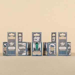 May include: A set of seven small, blue and gold boxes with a variety of designs. The boxes are arranged in a row on a beige surface. The boxes have a vintage aesthetic and feature a variety of designs, including a compass, a key, and a lock.