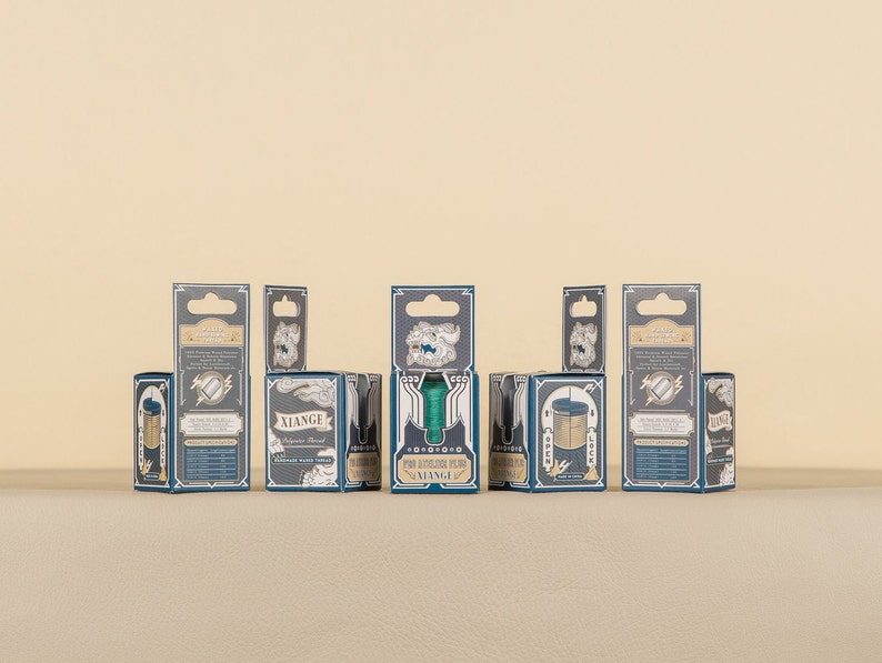 May include: A set of seven small, blue and gold boxes with a variety of designs. The boxes are arranged in a row on a beige surface. The boxes have a vintage aesthetic and feature a variety of designs, including a compass, a key, and a lock.