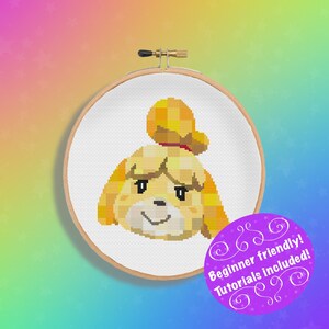 May include: Cross stitch pattern of a yellow dog with a brown nose and brown eyes. The dog is wearing a red bow. The pattern is in a wooden embroidery hoop. The text "Beginner friendly! Tutorials included!" is on a purple background.