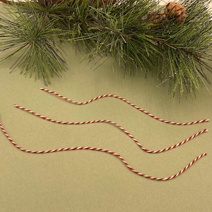 May include: Three red and white striped twine strings on a brown surface.