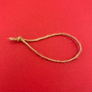 May include: A length of natural twine tied into a loop on a red background.