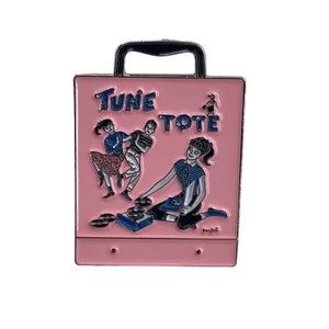 Può includere: Uno spillo in metallo rosa a forma di valigetta vintage per dischi con maniglia. La valigetta ha le parole "Tune Tote" stampate sul davanti. La valigetta presenta un'immagine di cartoni animati di tre persone che ballano e suonano dischi.