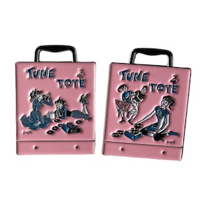 Può includere: Due spille in smalto rosa a forma di borse della spesa con il testo "Tune Tote" e illustrazioni di persone che ascoltano dischi.