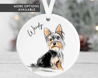 May include: White ceramic ornament with a hand-drawn illustration of a Yorkshire Terrier dog. The dog is black, brown, and tan with a white chest. The ornament has the name "Woody" written on it.