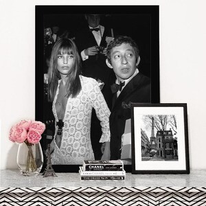 May include: Black and white photograph of a couple in a formal setting. The woman is wearing a white lace dress and the man is wearing a suit and bow tie. The photo is framed in a black frame and is displayed on a shelf with a small Eiffel Tower figurine and a stack of books.