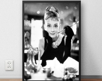 May include: Black and white photograph of a woman wearing a black dress and a pearl necklace. She is holding a cigarette in her hand and looking at the camera.