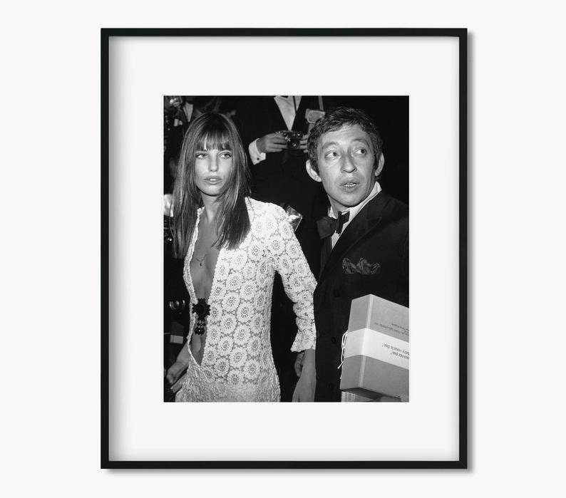 May include: A black and white photograph of a woman wearing a white lace dress and a man wearing a suit and bow tie. The man is holding a box in his right hand.