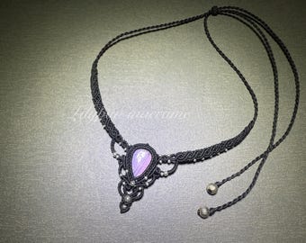 May include: A black macrame necklace with a teardrop-shaped pendant. The pendant features a light purple stone and is accented with small silver beads. The necklace has adjustable ties with silver ball ends.