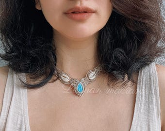 May include: A handcrafted macrame necklace featuring a teardrop-shaped turquoise stone pendant. The necklace incorporates white shells and intricate knotting details. The text "Loran macrame" is visible on the necklace.